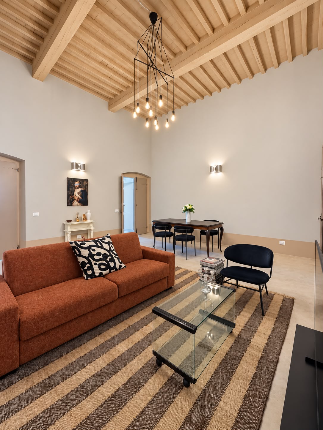 Zona pranzo del living: soffitto a travi a vista, tavolo antico con sedie e ingressi ad arco verso gli altri ambienti.
