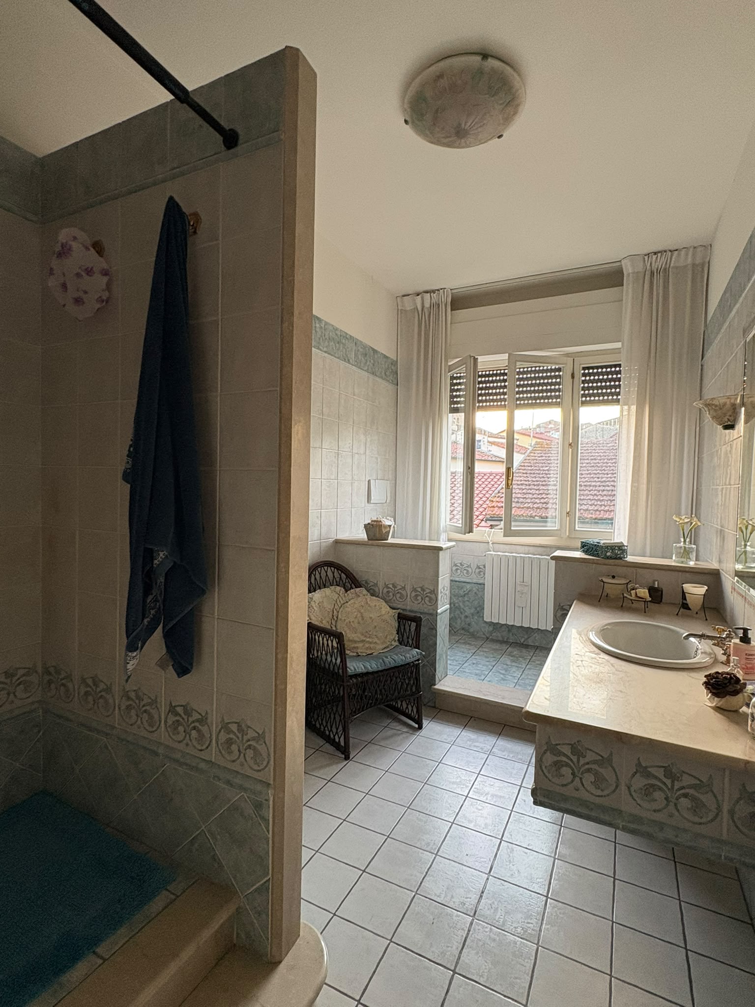 Secondo bagno con doccia separata, ampio piano lavabo e finestra con vista sui tetti del centro.
