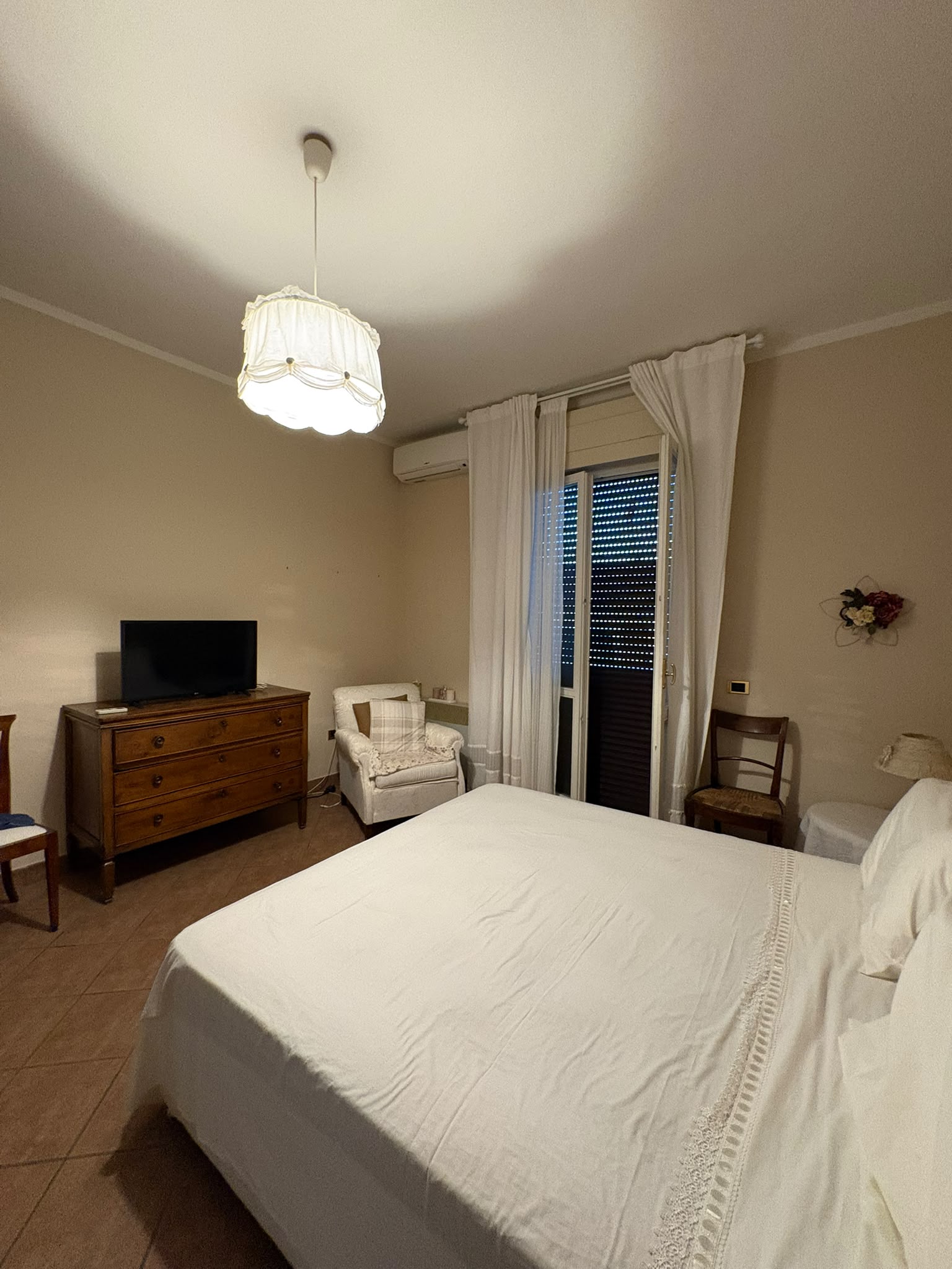 Camera matrimoniale con letto grande, comò in legno, aria condizionata e portafinestra sul balcone.
