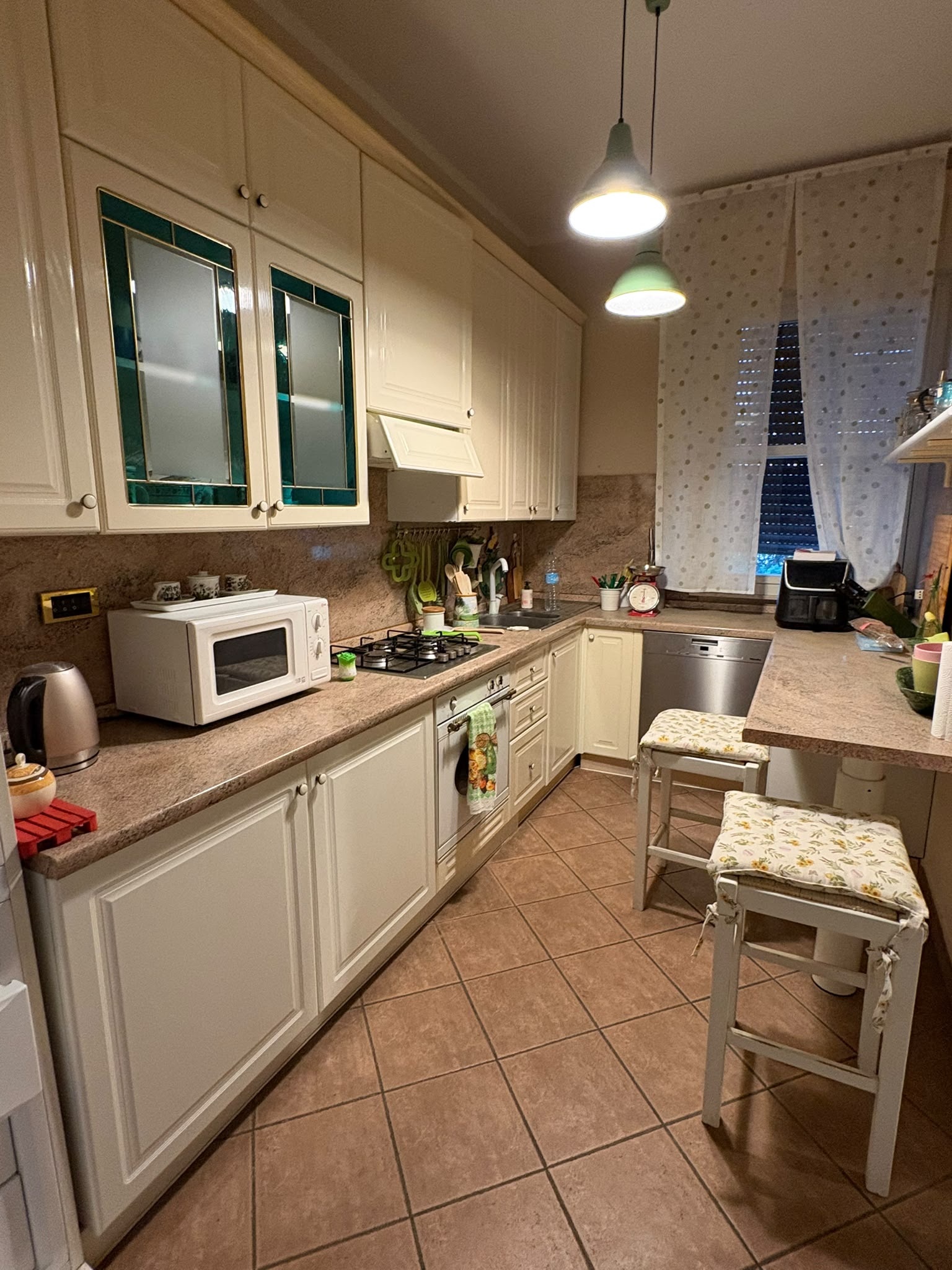 Cucina abitabile con mobili chiari, piano cottura a gas, forno, lavastoviglie e penisola con sgabelli.