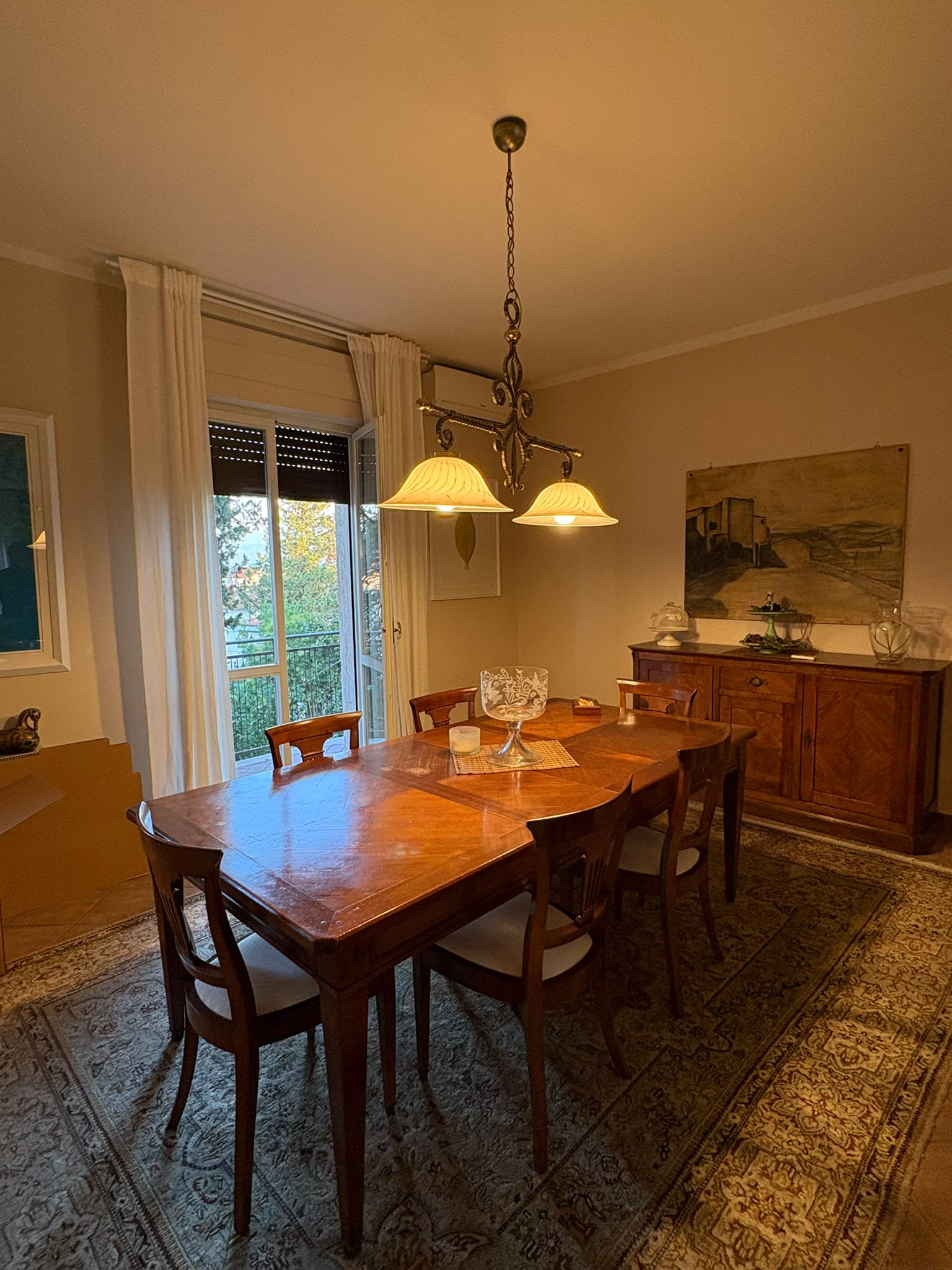 Sala da pranzo con tavolo in legno da sei posti, credenza e portafinestra sul balcone.