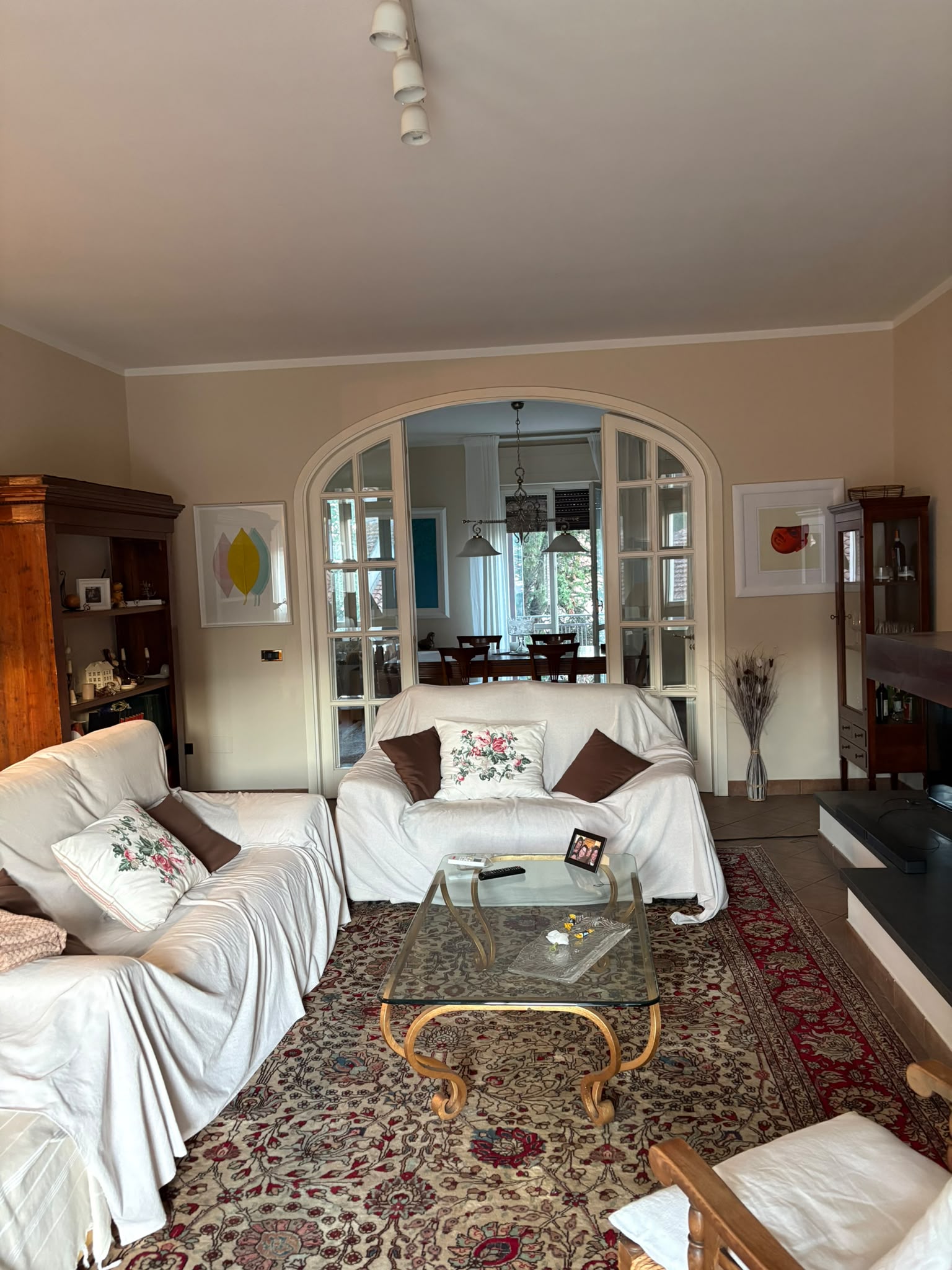 Salone con due divani, tappeto e camino, collegato alla sala da pranzo da una porta ad arco a vetri.