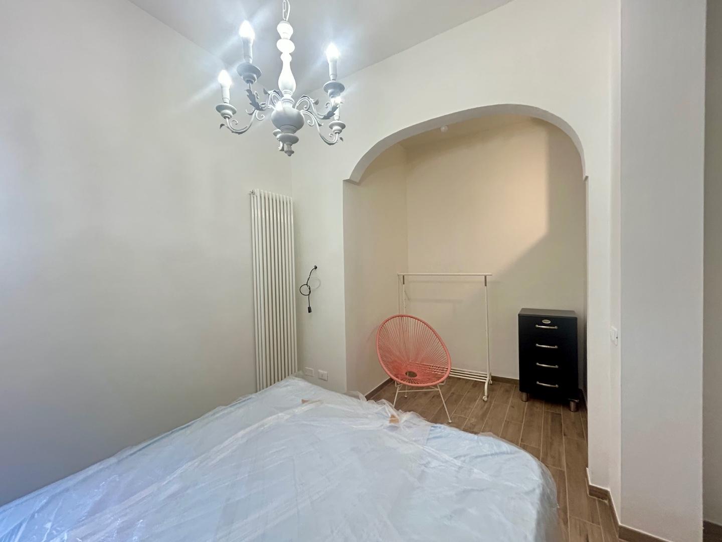 Camera da letto con nicchia adibita ad armadio a giorno, cassettiera e termosifone.