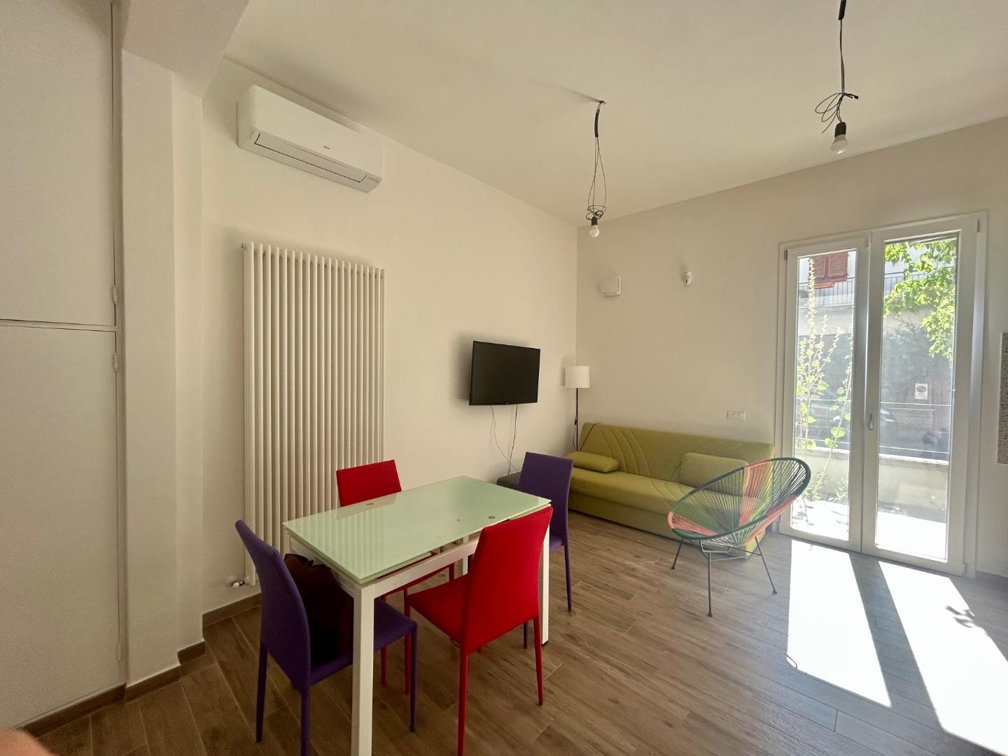 Soggiorno del bilocale in affitto a Empoli, zona Ponzano: divano, tavolo da pranzo e porta finestra che affaccia sul resede privato.