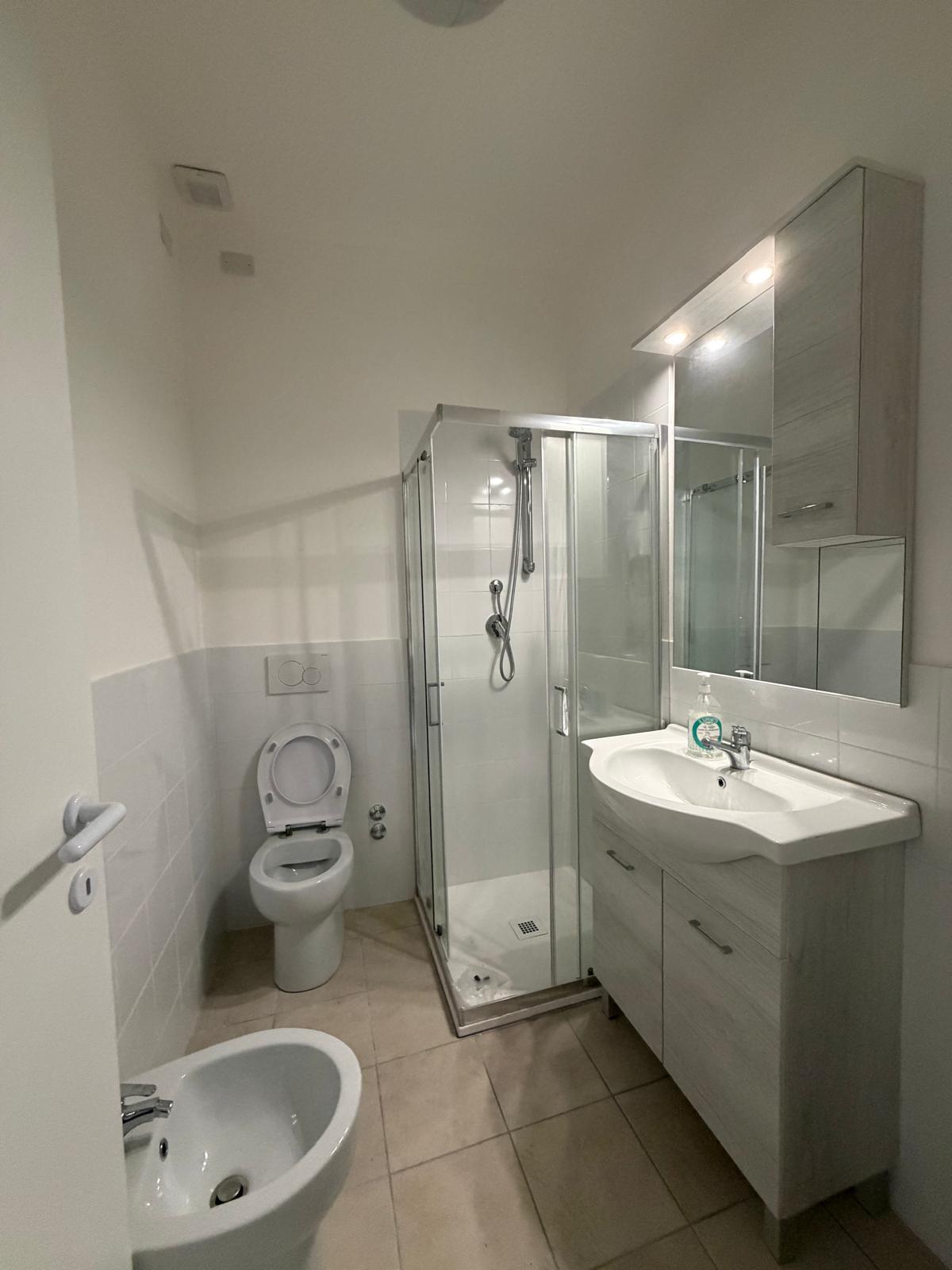Bagno ristrutturato con box doccia in cristallo, mobile lavabo con specchio contenitore, sanitari e bidet.