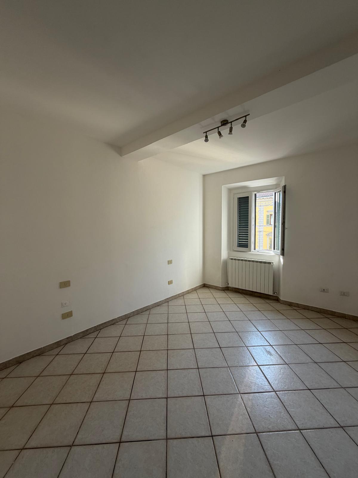 Camera del bilocale: ambiente ampio e luminoso, pareti bianche, faretti a soffitto e finestra affacciata sul centro storico.